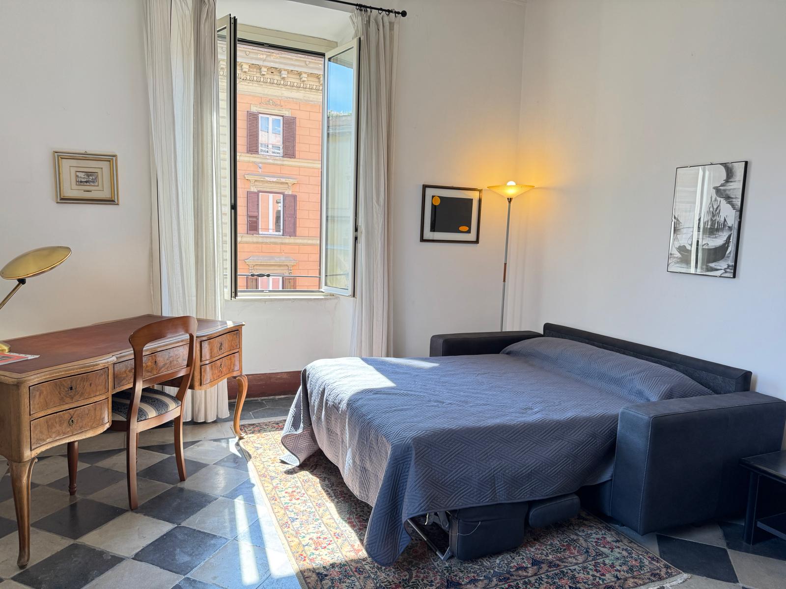 Camera con divano letto blu navy convertibile, scrivania antica, tappeto persiano e vista sui palazzi romani
