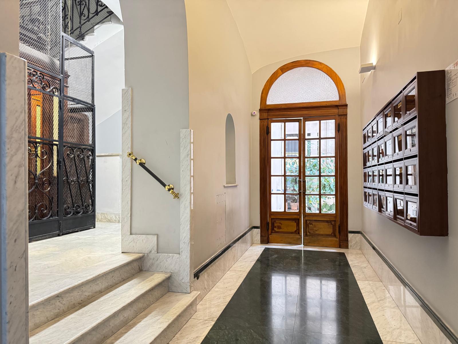 Elegante ingresso del palazzo con scale in marmo, ascensore storico, porta ad arco in legno e cassette postali
