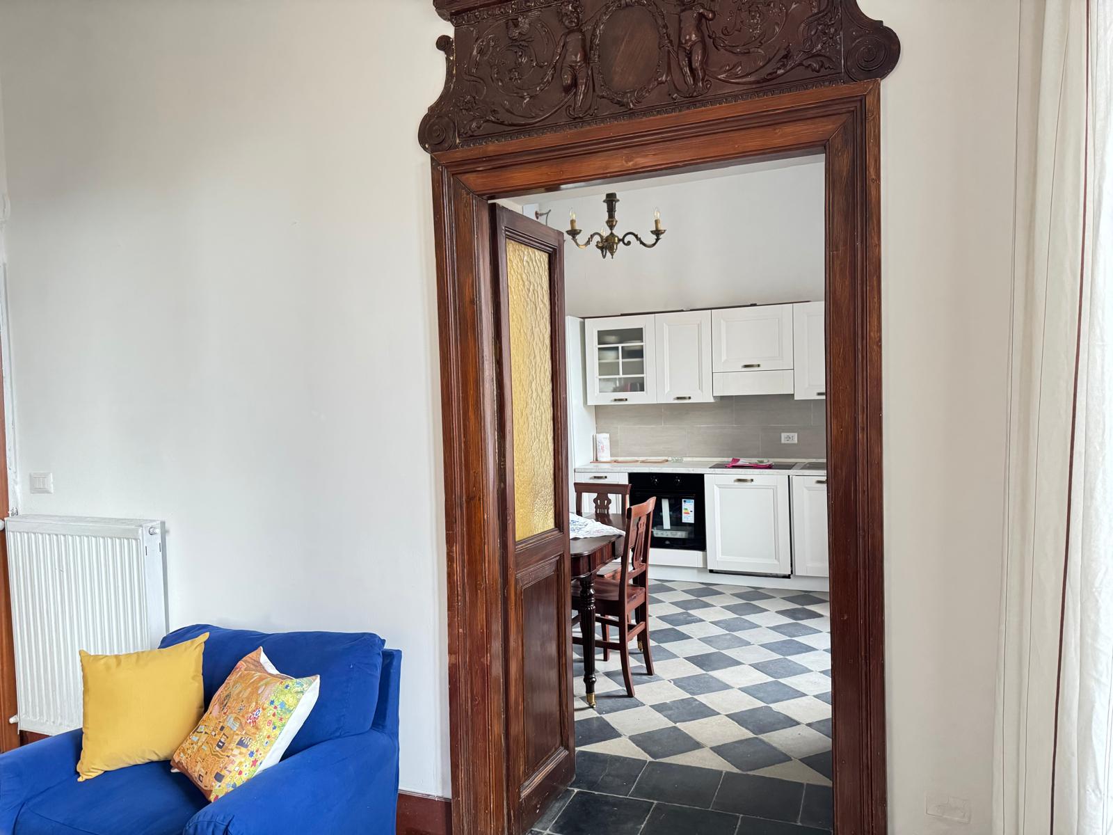 Vista dal soggiorno attraverso elegante porta ad arco intagliata verso la cucina moderna bianca, con divano blu in primo piano