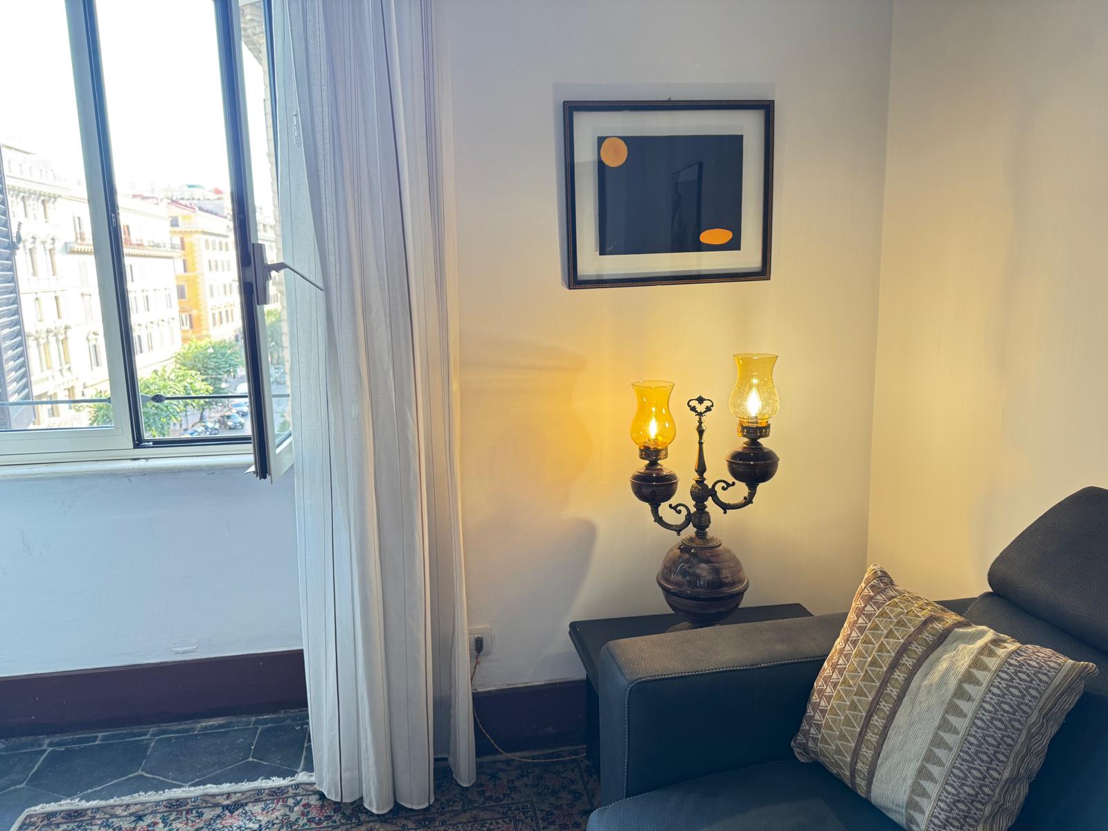 Dettaglio soggiorno con lampada ad olio vintage, divano blu navy, cuscini geometrici e quadri incorniciati
