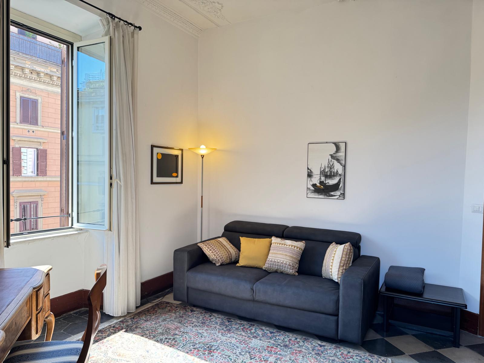 Soggiorno con divano blu navy, zona scrivania, tappeto persiano e vista sull'architettura romana