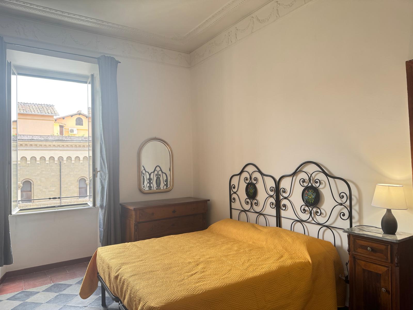 Camera matrimoniale con vista spettacolare su torre storica romana, testiera in ferro battuto decorata e comodini in legno