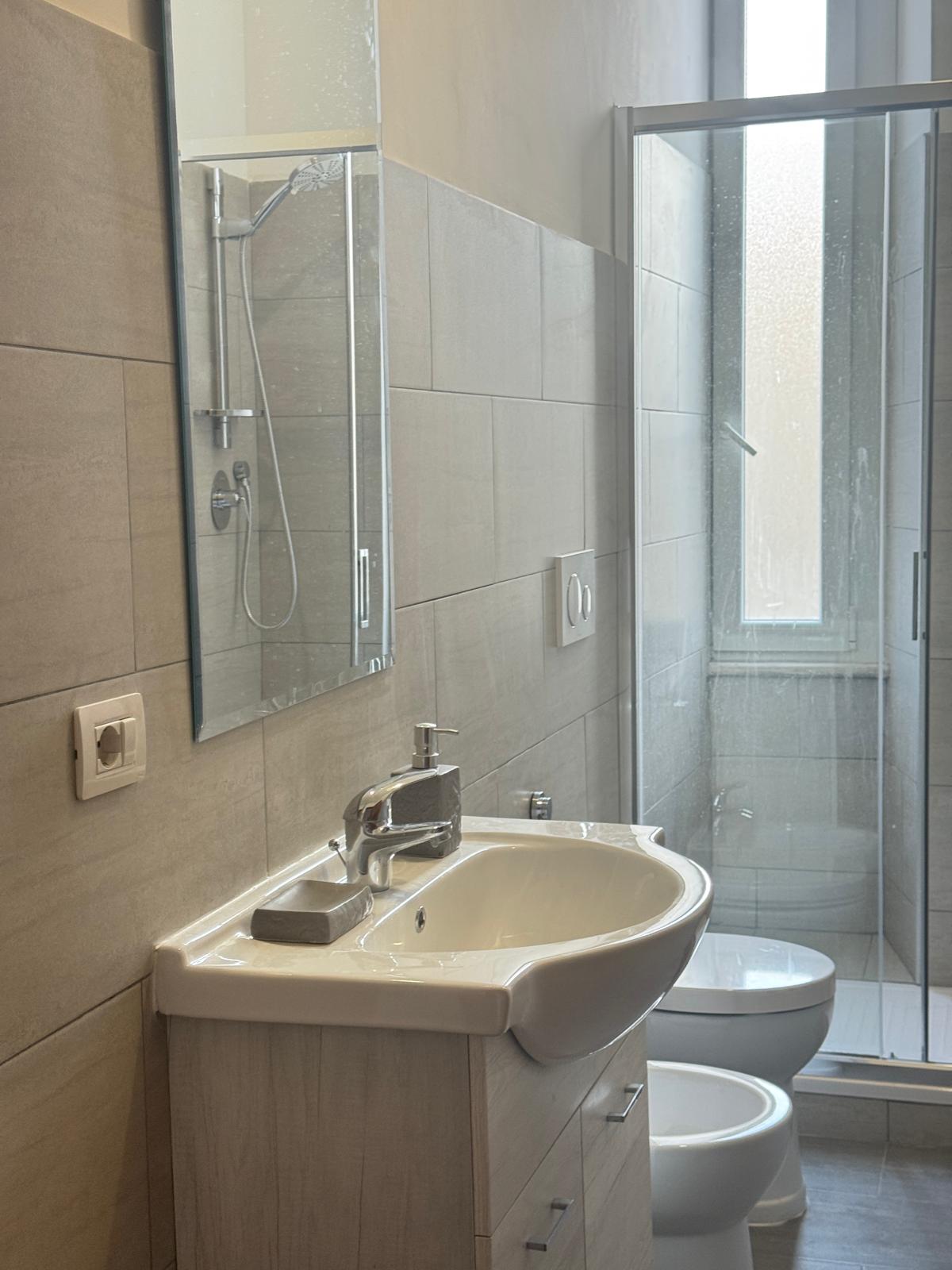Bagno moderno con piastrelle beige, box doccia in vetro, sanitari bianchi e bidet