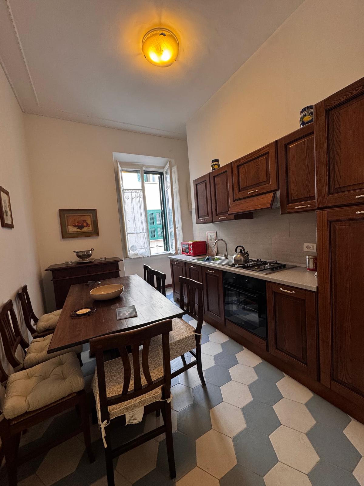 Cucina tradizionale con mobili in legno scuro, pavimento esagonale, tavolo da pranzo e vista sulla strada romana