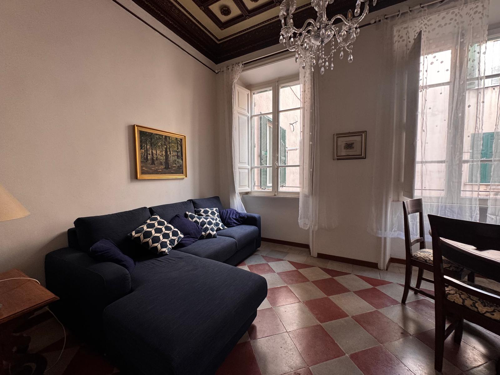 Soggiorno elegante con divano ad angolo blu navy, soffitto decorativo con modanature, lampadario di cristallo e vista sui palazzi romani