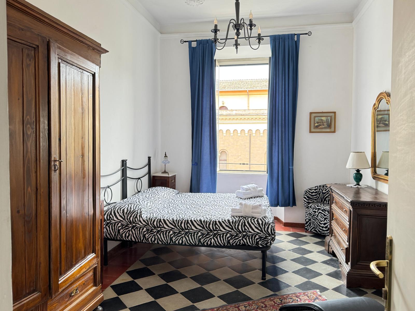 Camera matrimoniale con biancheria zebrata, letto in ferro battuto, grande armadio in legno e vista spettacolare sull'architettura romana