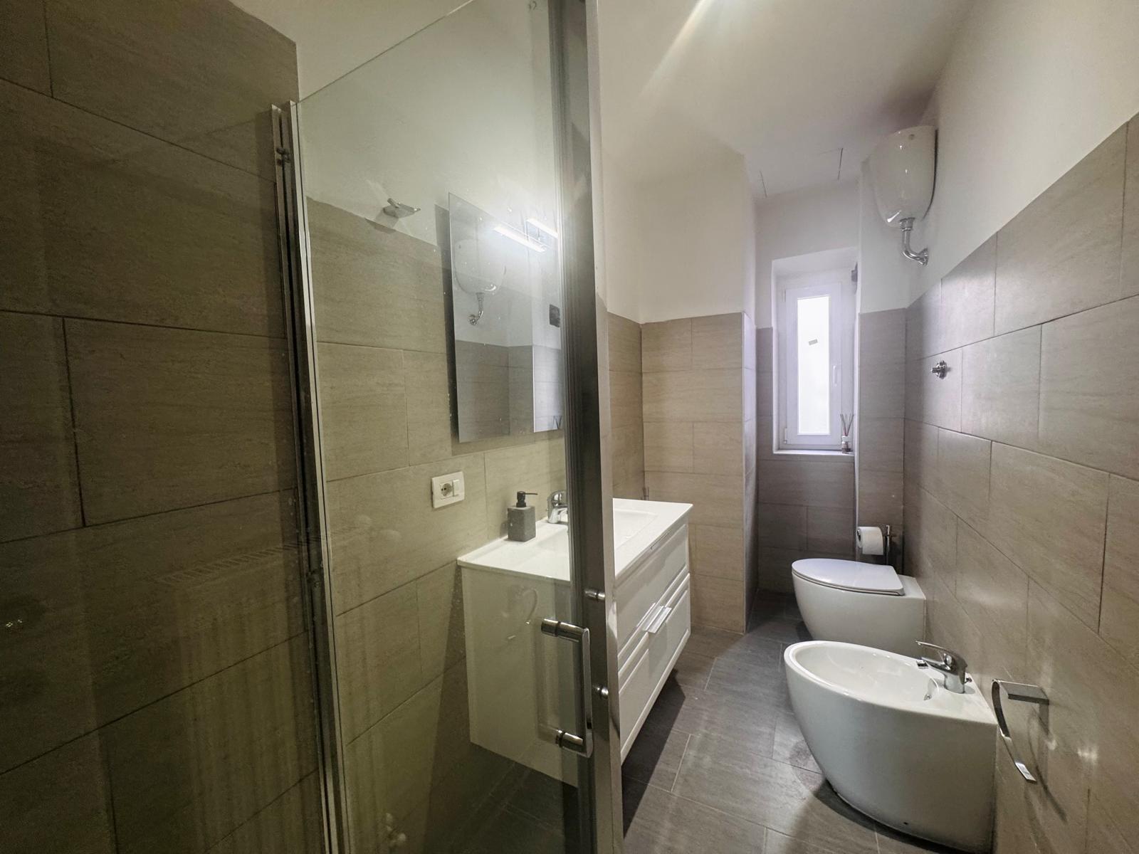 Bagno moderno con piastrelle grigie, box doccia in vetro, mobile sospeso bianco e sanitari contemporanei